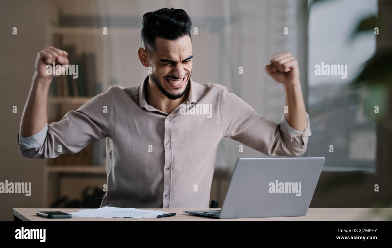 Junge erfolgreiche fröhlich hispanischen Mann männlichen Investor Geschäftsmann halten Dokument Blick auf Laptop gewinnen online Lotterie feiern Sieg erhalten neue Distanz Job Stockfoto
