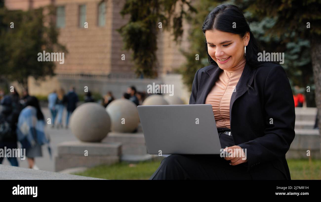 Junge Geschäftsfrau Freiberufler Student sitzt im Freien Lesen E-Mail auf Laptop lächelnd Lachen gute Nachrichten fühlt sich glücklich genießt Prozess surfen Web auf Stockfoto