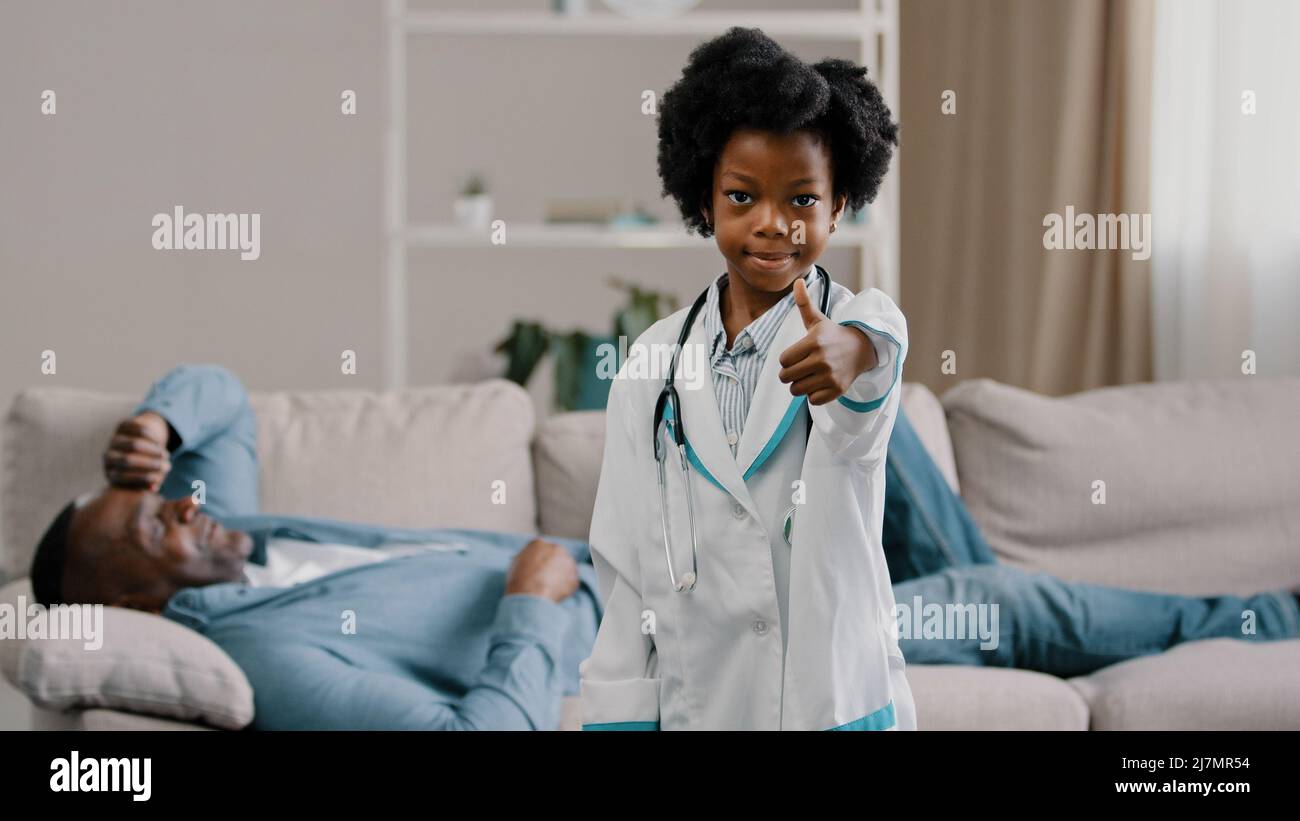 Kleine afroamerikanische Tochter, die mit Vater Vater Patient auf der Couch liegend spielt, Kind Mädchen, das vorgibt, Arzt zu sein und die Kamera lächelnd ansieht Stockfoto