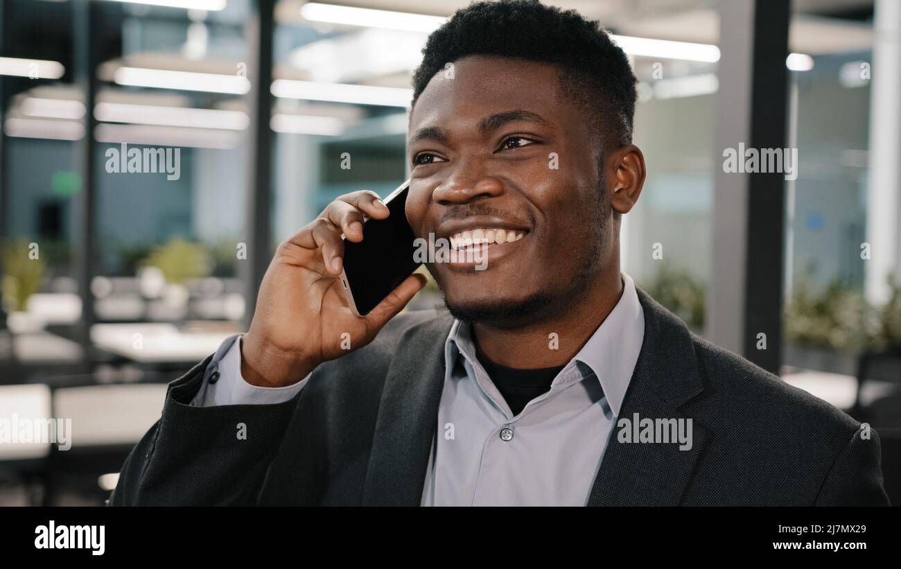 Afrikanischer Geschäftsanalyst Manager lächelnder Mann, der am Handy Kundenberatung spricht und in Innenräumen emotional Geschichten erzählt, die online gemacht werden Stockfoto