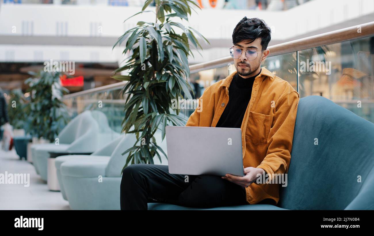 Junge seriöse arabische männliche Freiberufler in Brille sitzt Blick auf Laptop-Bildschirm funktioniert aus der Ferne geladen in Gedanken über die Arbeit denkt über Geschäftsproblem Stockfoto