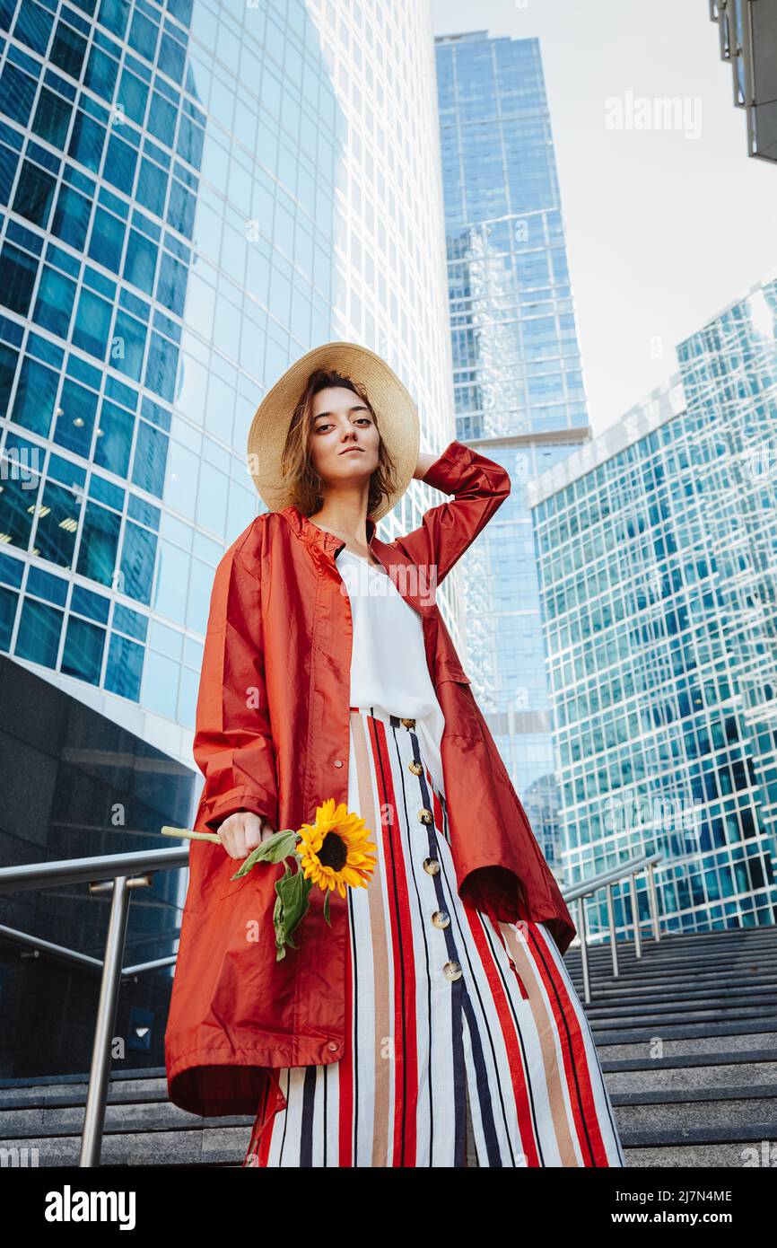 Selbstbewusste Geschäftsfrau wartet auf Treffen oder Datum, Frau in Mode-Kleidung mit Sonnenblume steht im Finanzzentrum. Geschäftsfrau, Konzept o Stockfoto