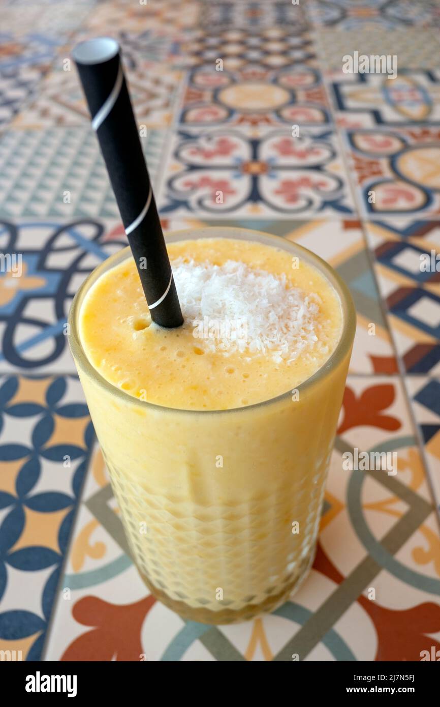 Großes Glas frisch zubereiteter Ananas und Mango-Smoothie mit Kokosflocken auf der Oberseite und einem Papierstroh für einen einfachen, gesunden Fruchtdrink Stockfoto