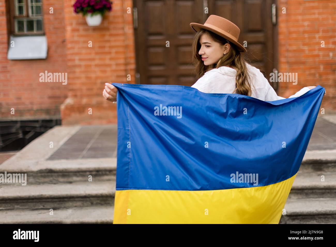 Schönes Mädchen in ukrainischer Flagge stehend besorgt über Krieg. Nette Frau fühlt emotionale Schmerzen, nachdem sie die Nachrichten gelesen hat. Freiheit und Patriot von Stockfoto