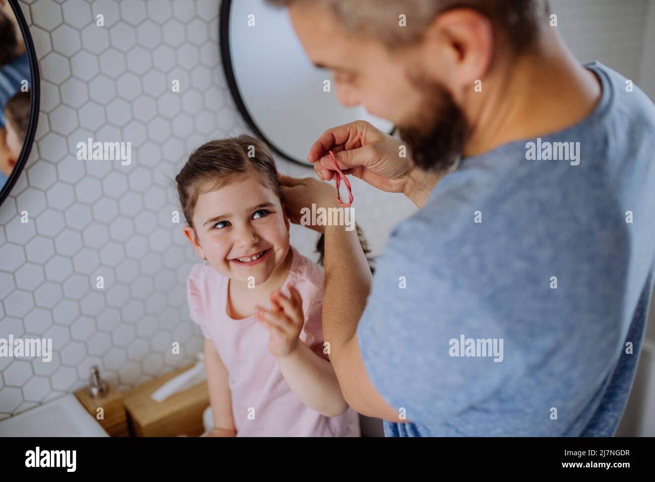 Vater putzt sich die Haare seiner kleinen Tochter im Badezimmer, morgendliches Routinekonzept. Stockfoto