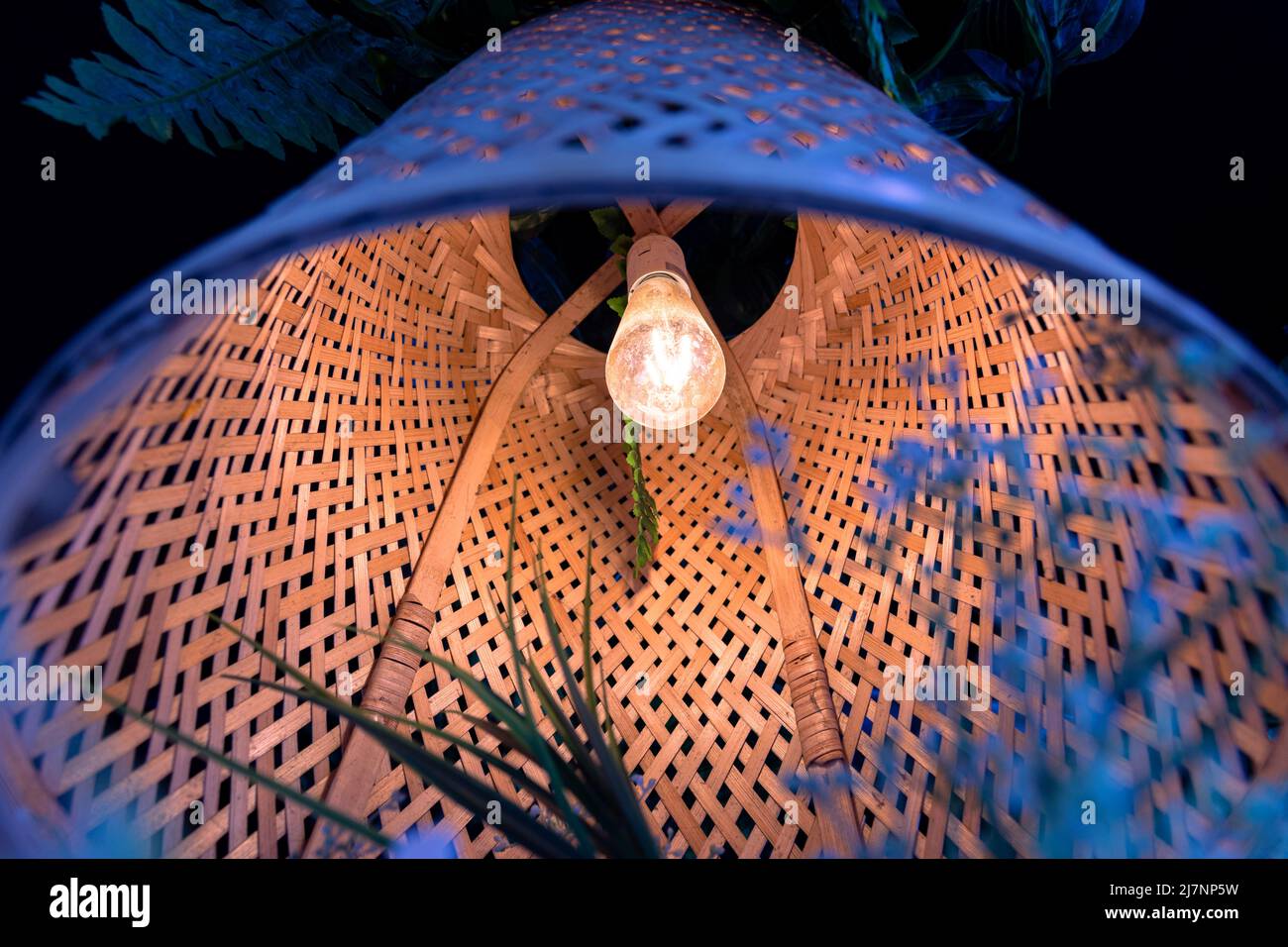 Eine Lampe mit einem Lampenschirm aus Korbholz, schöne Ansicht von unten. Gemütliche Atmosphäre, warmes Licht, umweltfreundliche Materialien. Stockfoto