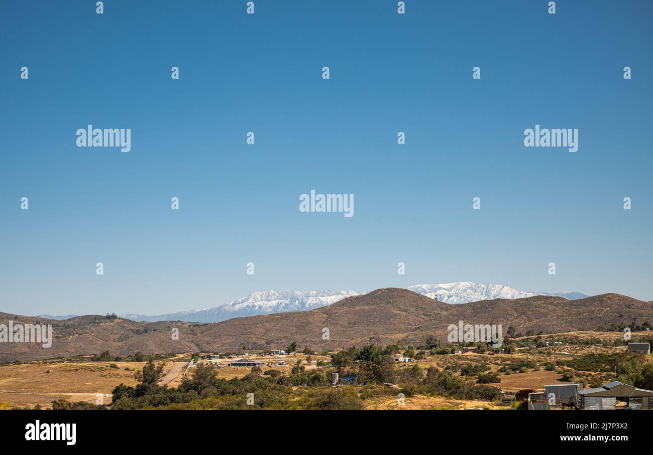 Temecula, CA, USA - 23. April 2022: Schneebedeckte San Jacinto-Berge, von der ländlichen Gegend nördlich von Temecula unter blauem Himmel, mit braunen Hügeln und y Stockfoto