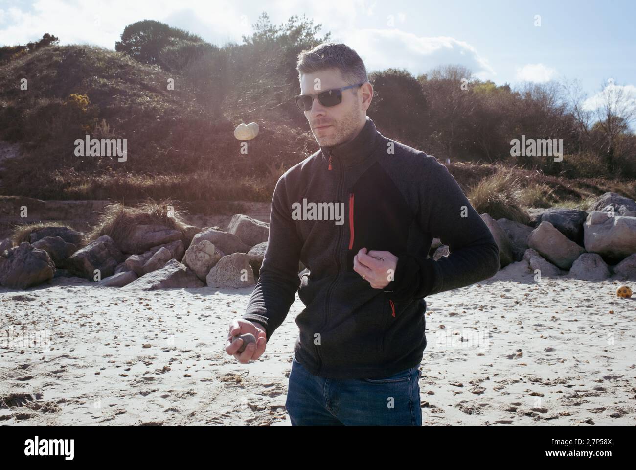Mann jongliert im Sommer gerne mit Steinen am Strand Stockfoto