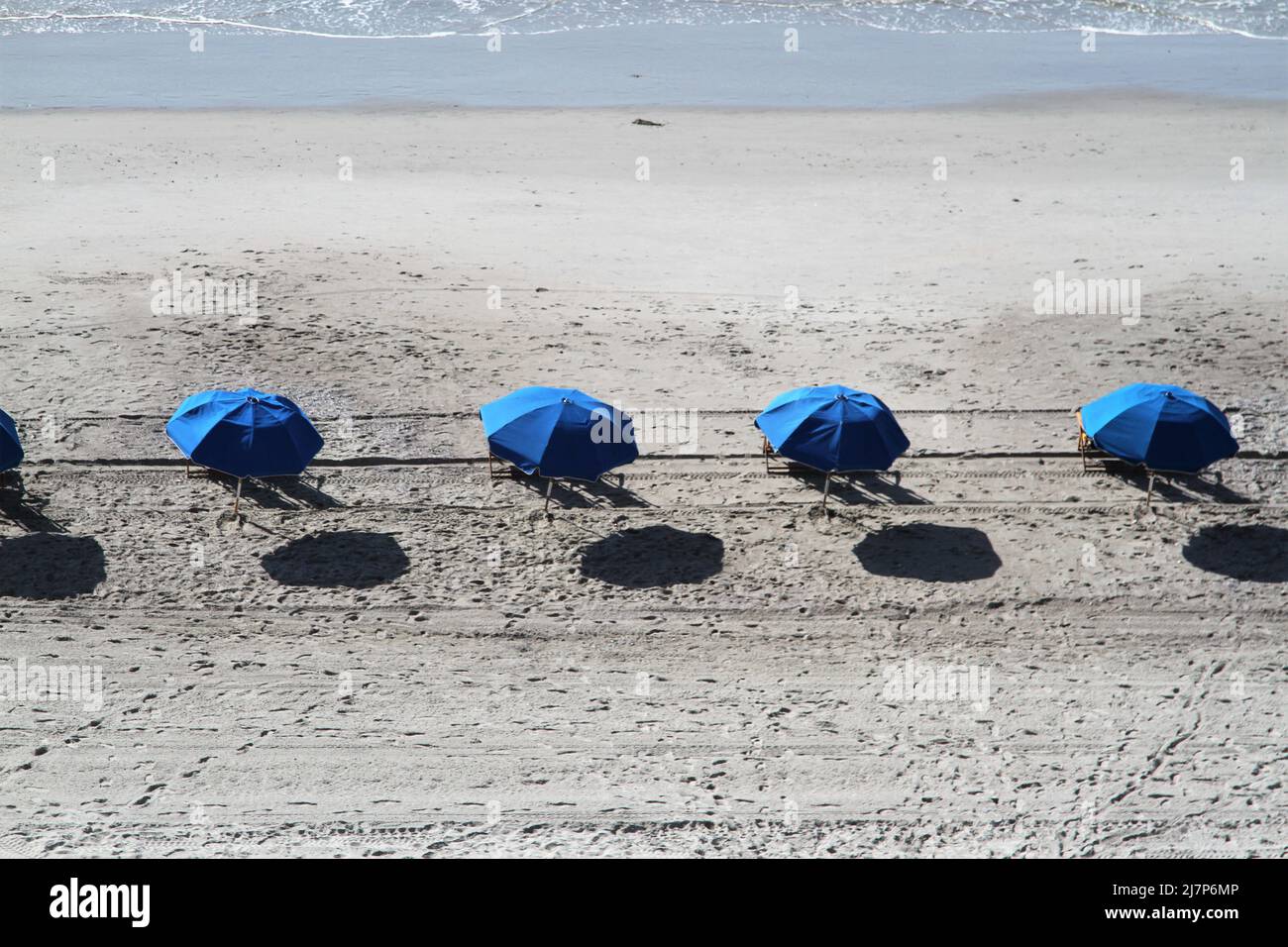 Strand mit blauen Sonnenschirmen mit Reflexen auf Sand Stockfoto