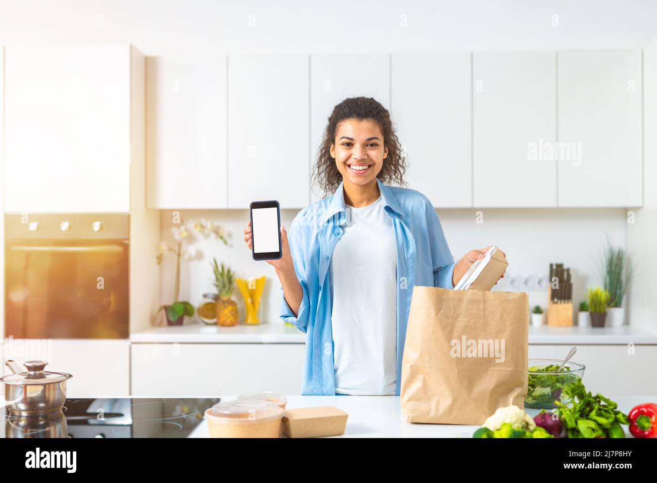 Lächelnde Frau mit einer Einkaufstasche, die online über das Smartphone bestellt und direkt zu Hause geliefert wurde Stockfoto