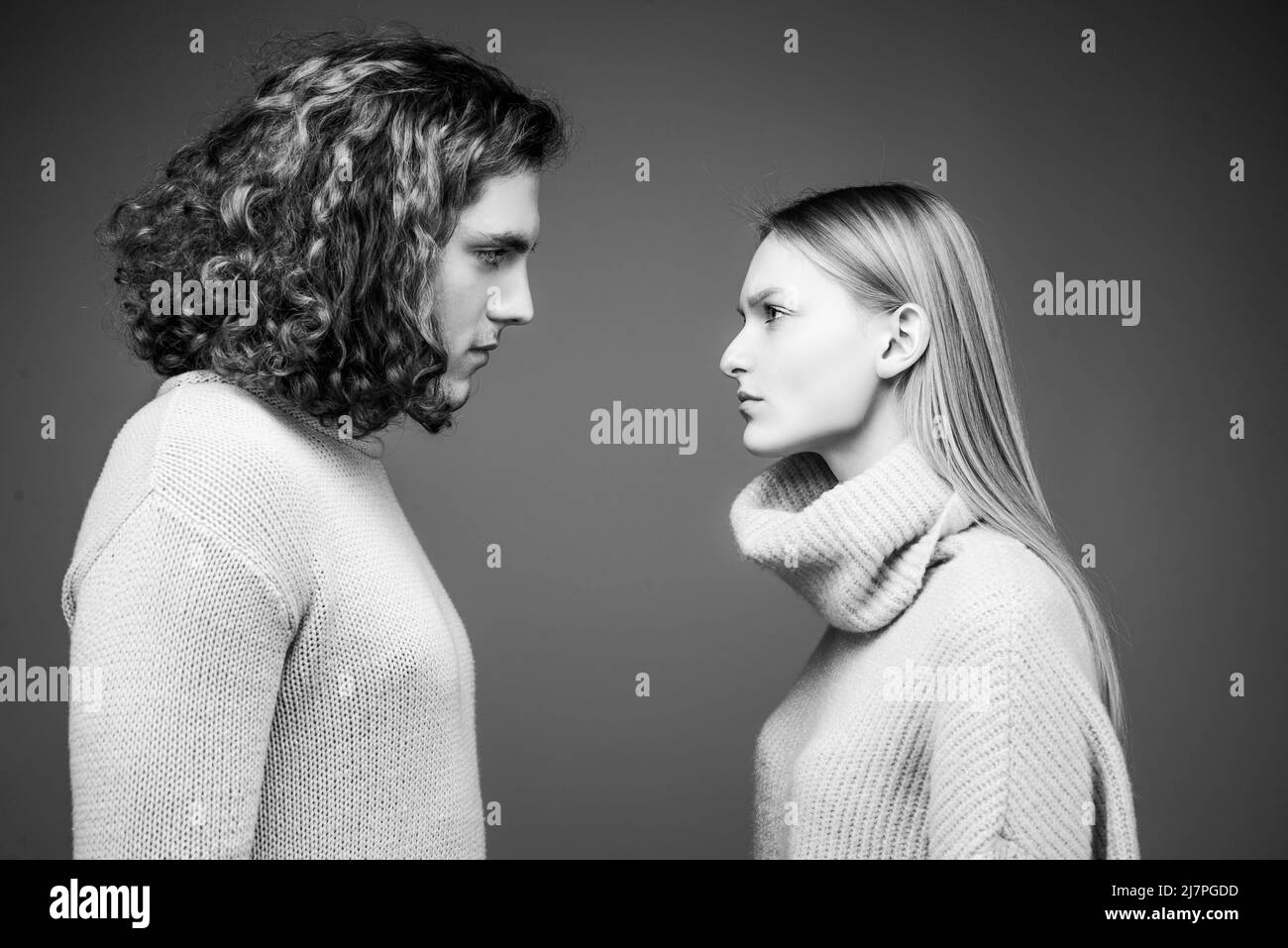Seitenansicht. Lockiger Mann und blonde Frau stehen einander gegenüber, Augen offen. Konzept der Konfrontation in der Familie. Ein Paar steht von Angesicht zu Angesicht mit einem Stockfoto