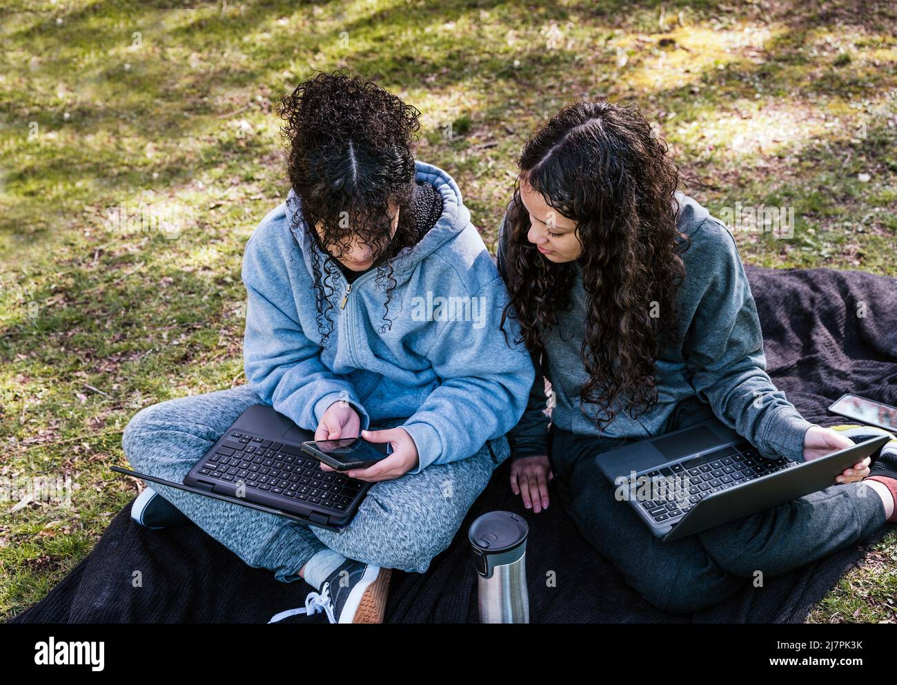 Portrait von fröhlichen Teenagerschwestern, Mädchen, die Mobiltelefon und Computer betrachten, während sie im Park sitzen. Stockfoto