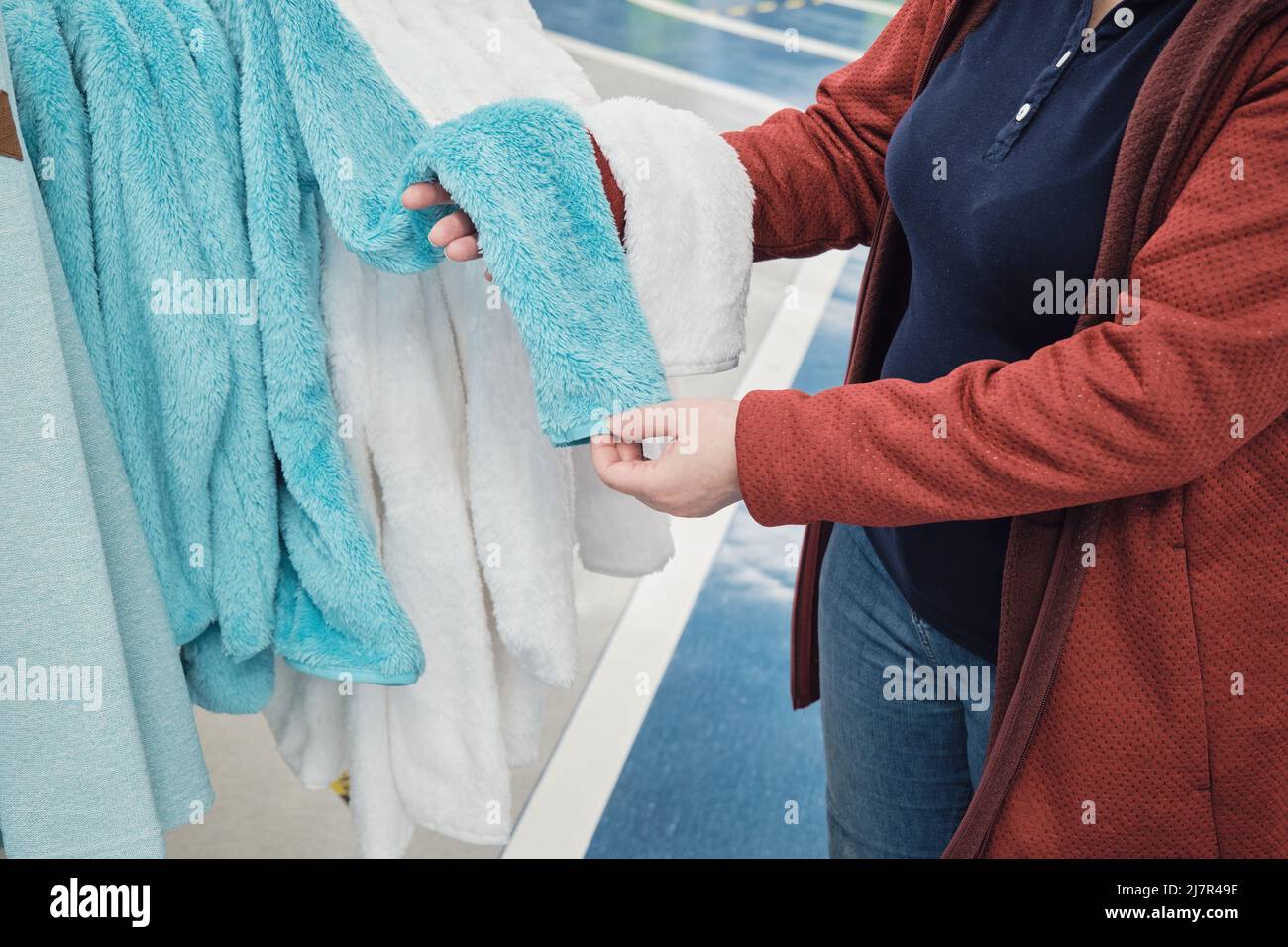 Eine Frau, die eine Maske gegen das Virus trägt, wählt eine weiche türkisfarbene Robe Stockfoto