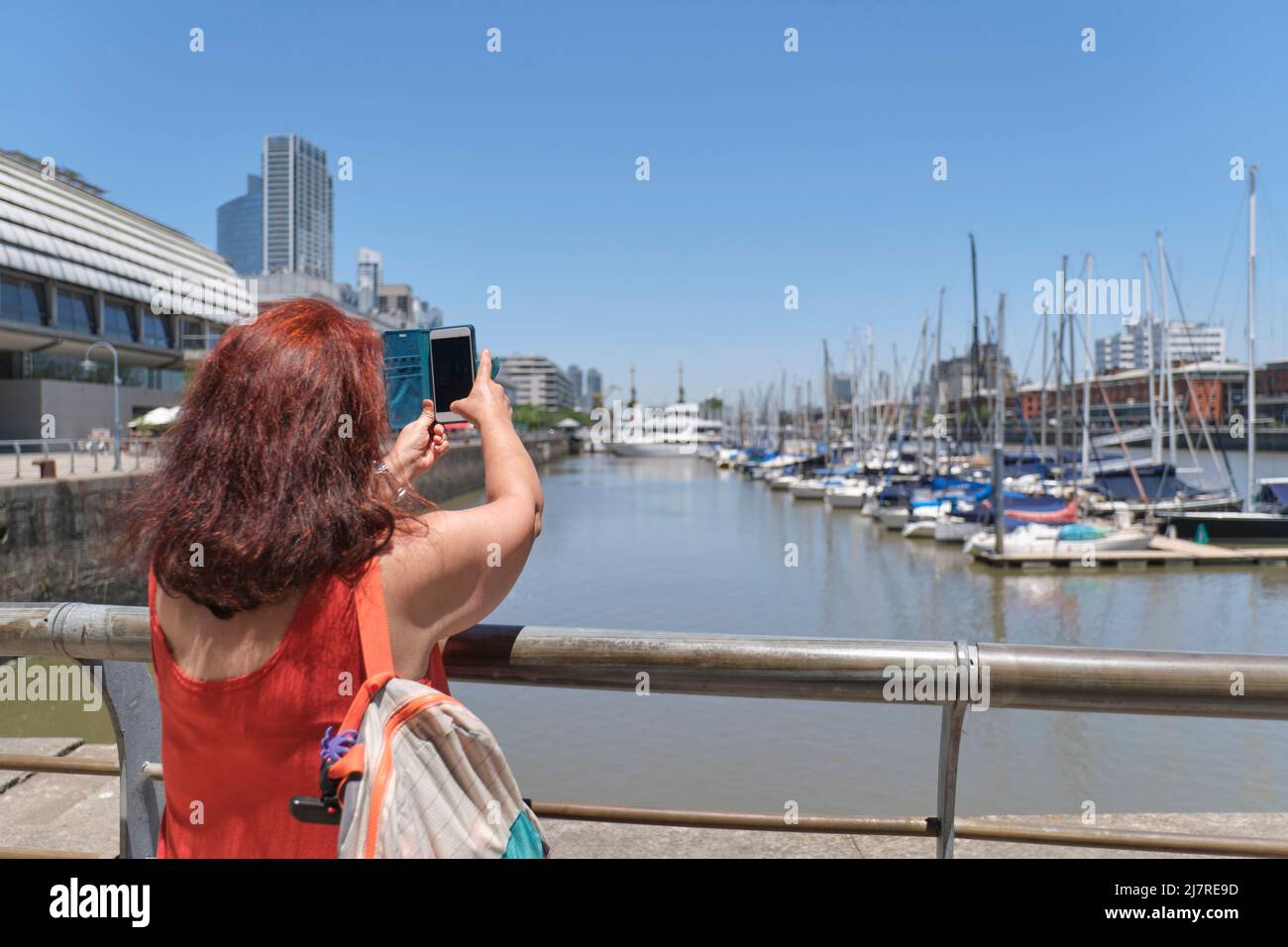 Weibliche Touristen von hinten gesehen, die an einem sonnigen Sommertag mit ihrem Telefon in Puerto Madero, in Buenos Aires, Argentinien, Fotos gemacht haben. Stockfoto