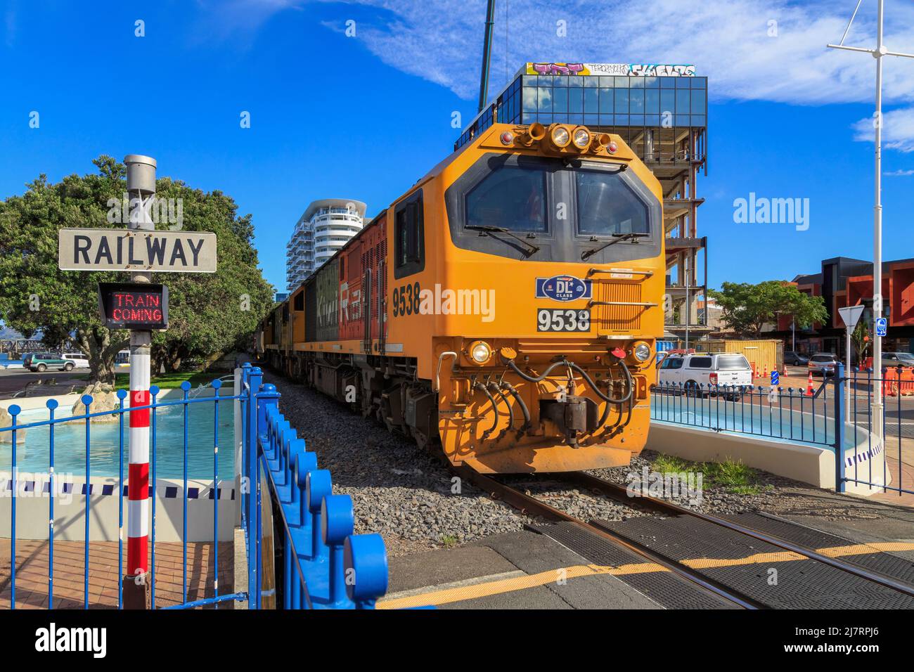 Eine Diesel-elektrische Lokomotive der KiwiRail DL-Klasse, die durch einen Bahnübergang in der Stadt Tauranga, Neuseeland, fährt Stockfoto