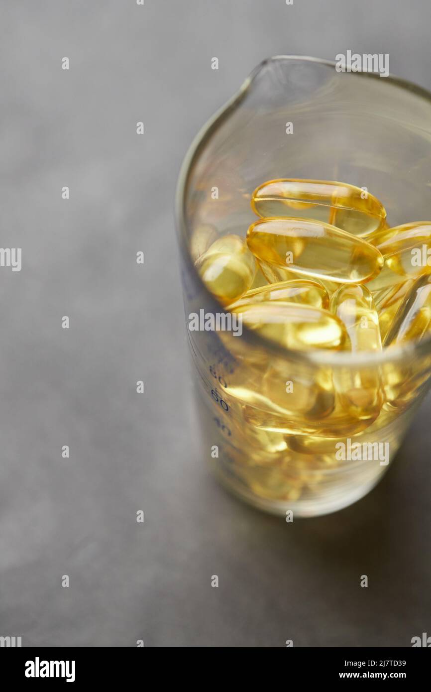 Omega-3-Fettsäurekapseln auf grauem Hintergrund in einem Glas. Das Konzept der Medizin und des gesunden Lebens. Vertikales Foto. Stockfoto