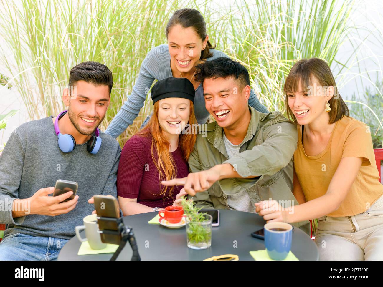 Eine Gruppe reizender, vielfältiger Menschen, die im Straßencafé am Tisch sitzen und während eines Videochats mit Freunden sprechen Stockfoto