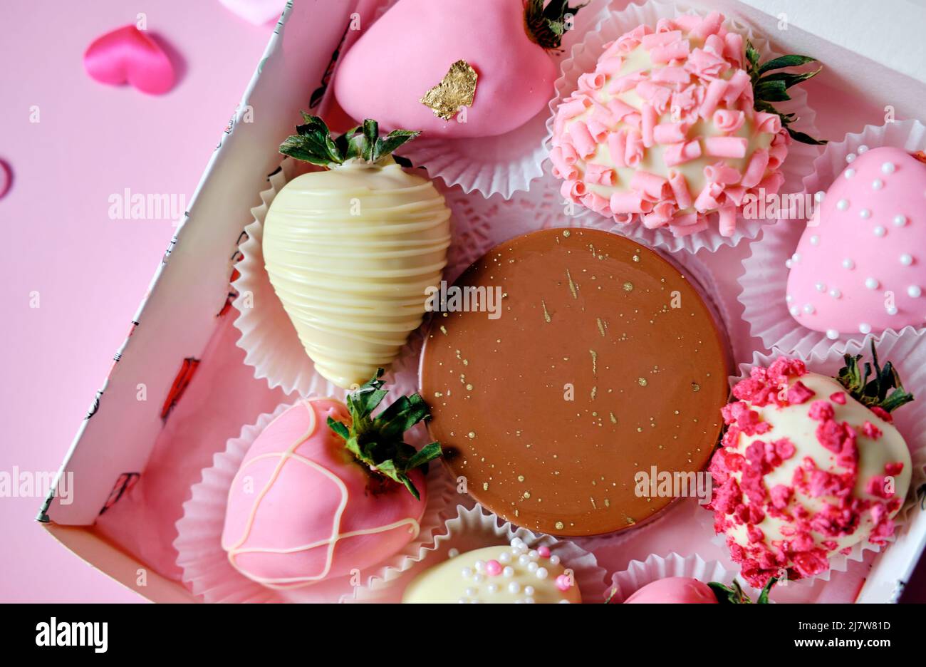 Erdbeeren in Schokolade in einer Schachtel mit verstreuten Herzen auf einem rosa Hintergrund. Süßes Geschenk zum Valentinstag Stockfoto