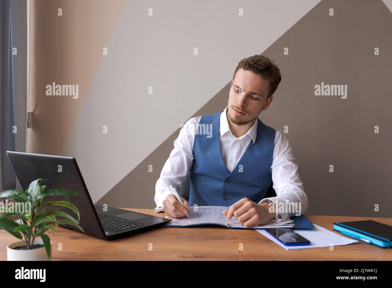 Geschäftsmann arbeitet in einem Büro mit Laptop und Dokumenten auf seinem Schreibtisch in Hemd und Weste mit Bart, ein Anwalt Berater. Das Konzept der erfolgreichen Menschen. Stockfoto
