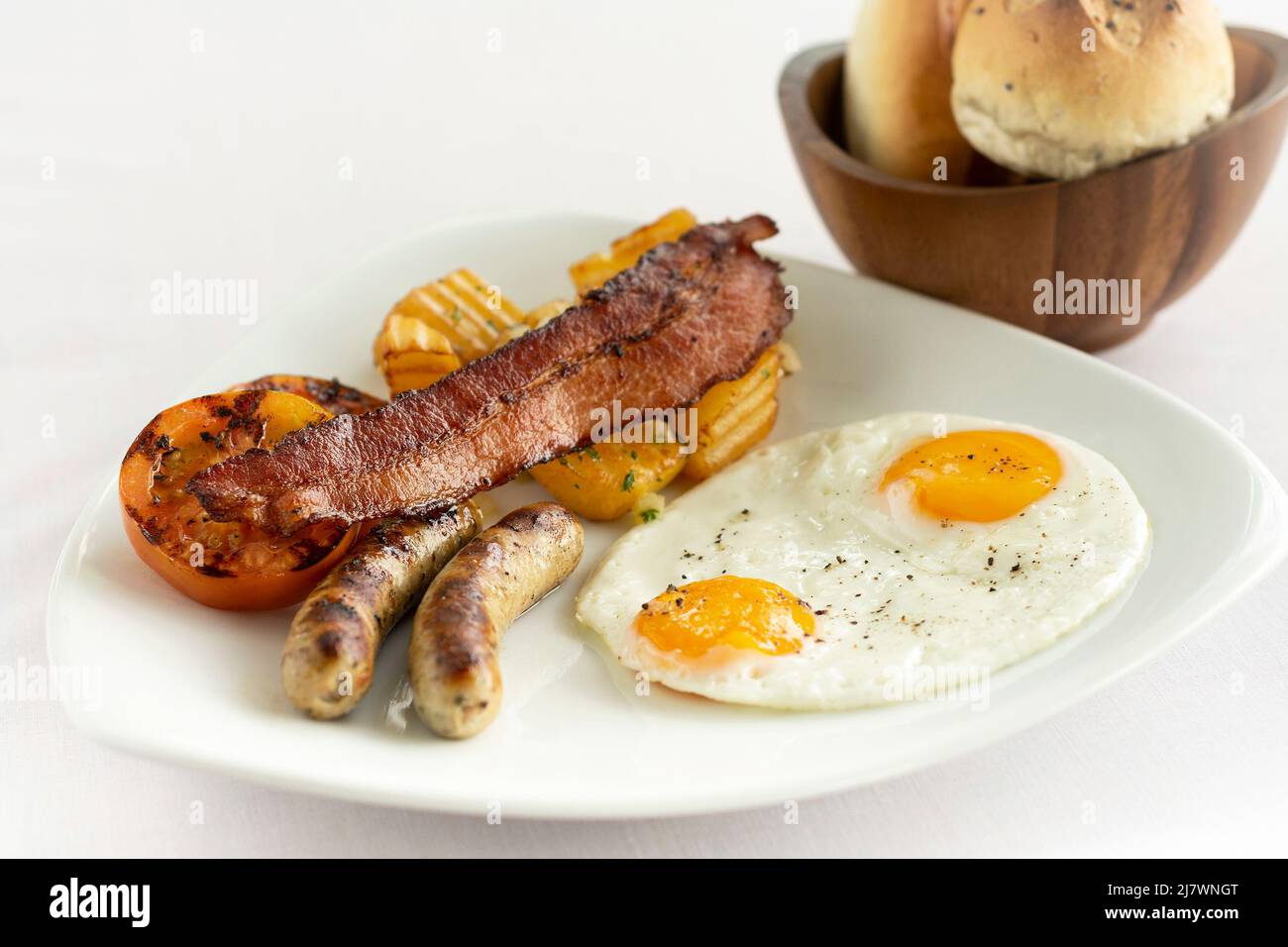 australisches Frühstück mit Spiegeleiern, Wurst, Speck und Kartoffeln auf weißem Hintergrund Stockfoto