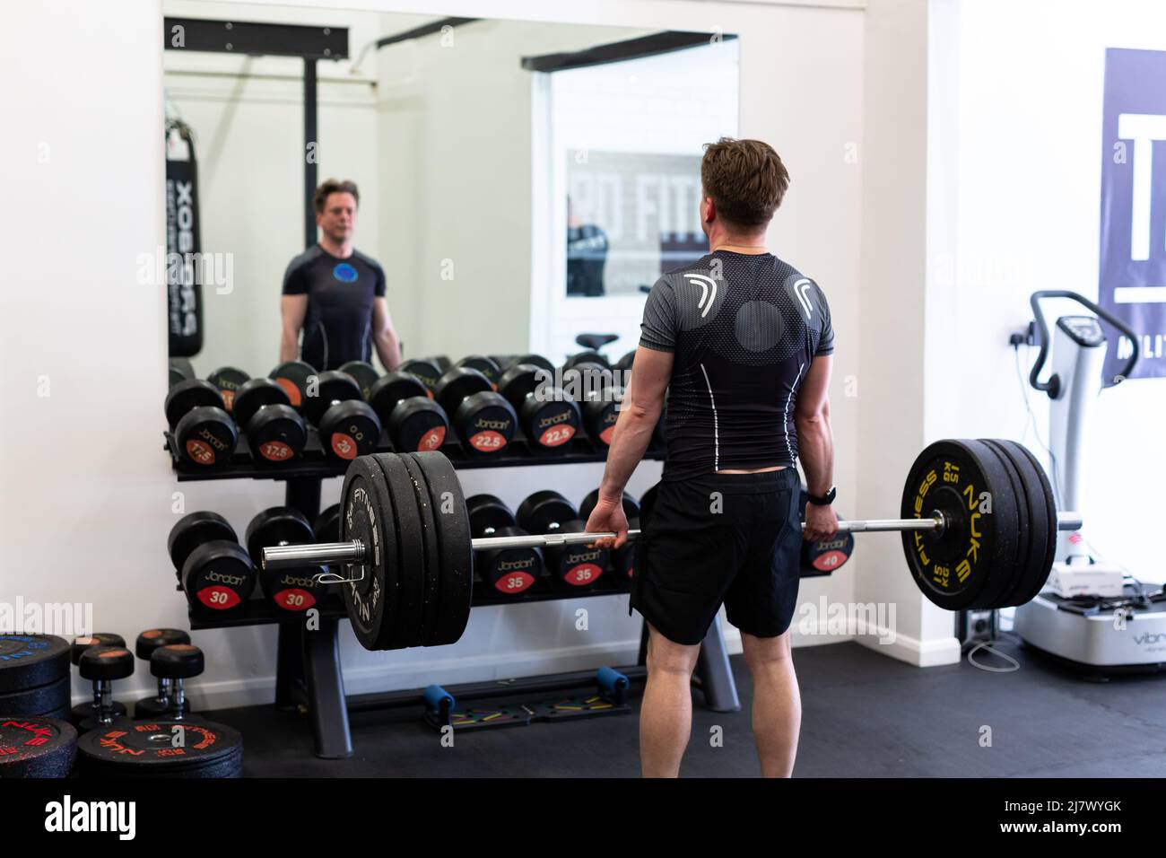 Ipswich Suffolk UK April 03 2022: Junger fittiger Mann macht in einem modernen Fitnessstudio einen Totzug. Sein Blick in den Spiegel, um seine Form zu überprüfen und zu heben Stockfoto