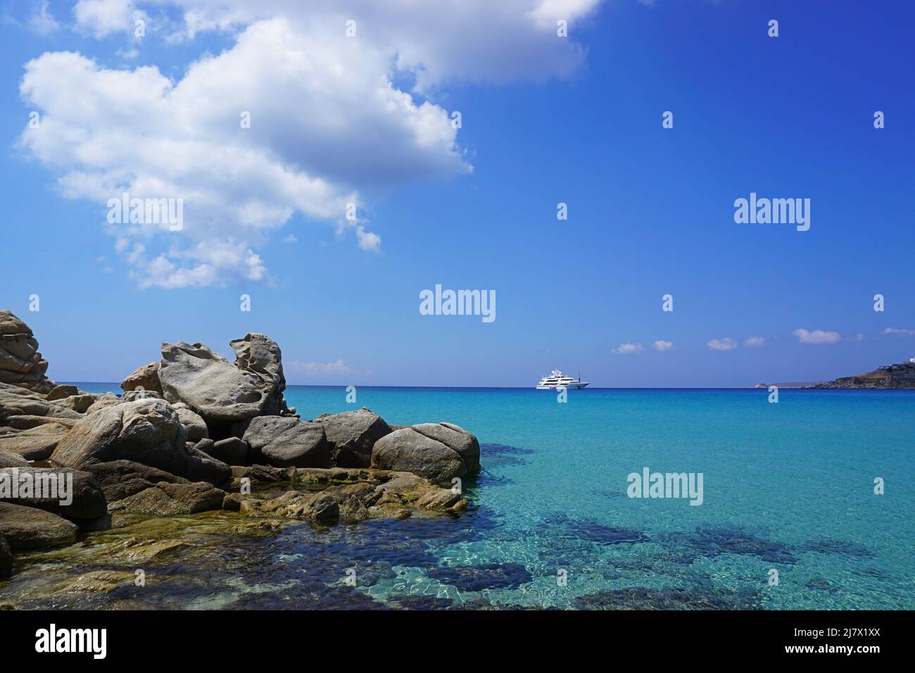 Eine blaue Postkarte von der Insel Mykonos: Das ruhige Mittelmeer in Platis Gialos, mit Yacht, blauem Himmel und weißen Wolken Stockfoto