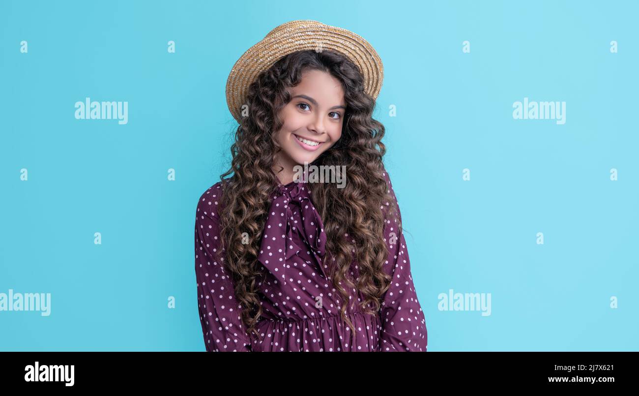 Kinderlächeln im Strohhut mit langen brünetten lockigen Haaren auf blauem Hintergrund Stockfoto