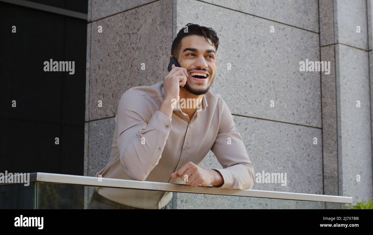 Porträt von fröhlich lächelnd sorglos glücklich hispanisch arabisch bärtig Geschäftsmann Chef Führer Kerl auf Balkon Terrasse stehen im Gespräch auf Handy Stockfoto