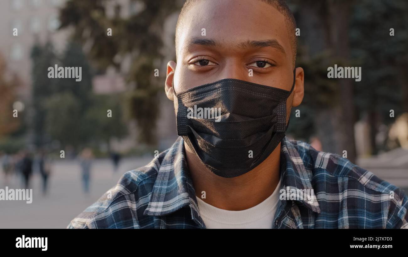 Nahaufnahme männlich Porträt afroamerikanischen Mann krank Kerl in medizinische Maske sitzt im Freien in der Stadt Straße in der Kamera in Quarantäne covid 19 Stockfoto