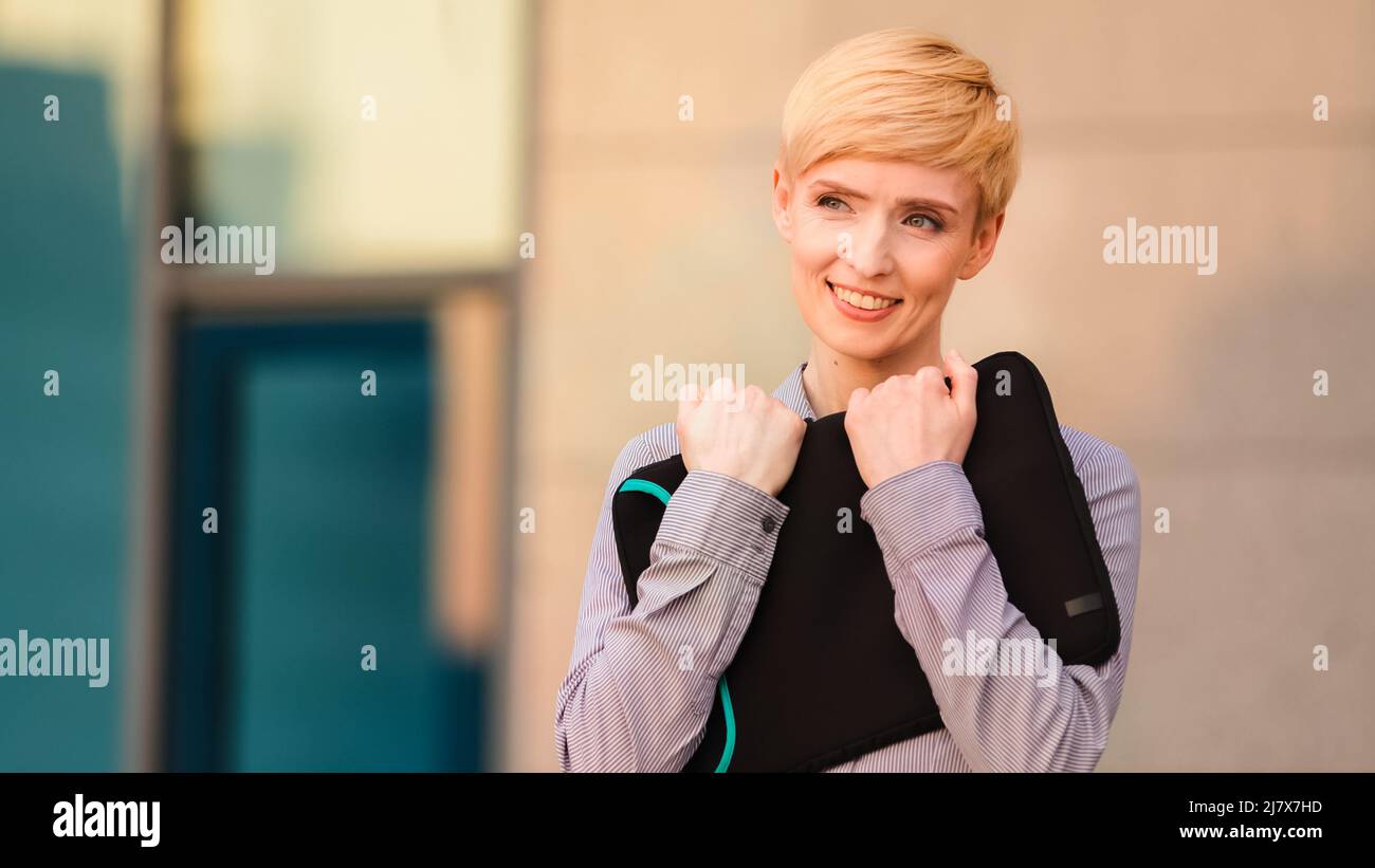 Glückliche reife Erwachsene Geschäftsfrau Chef Führer steht im Freien in der Nähe von Unternehmen Bürogebäude hält Laptop für den Fall Umarmungen umarmt Computer freut sich Stockfoto