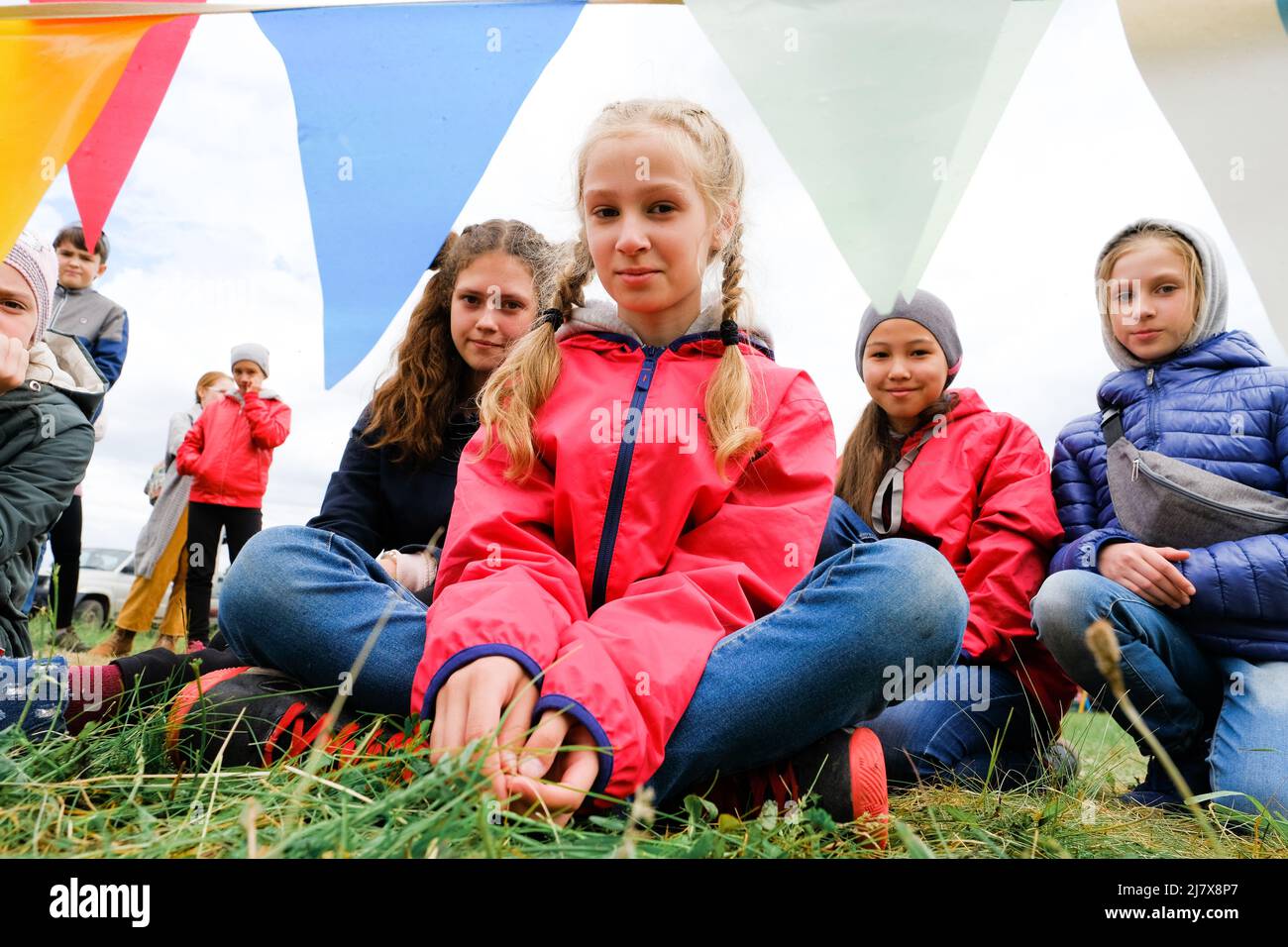 Russland, Tjumen, 15.06.2019. Eine Masse von Kindern unterschiedlichen Alters und Rennen sitzen auf dem Gras, in die Kamera schaut Stockfoto