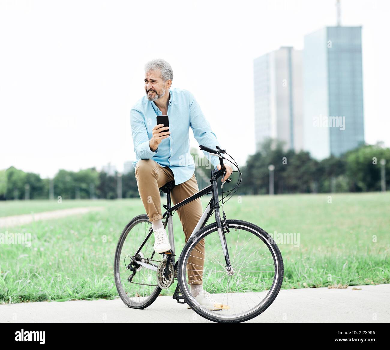 Senior Mann Smartphone Fahrrad Fahrrad Handy im Freien Stadtpark Geschäftsmann Business Casual Stockfoto