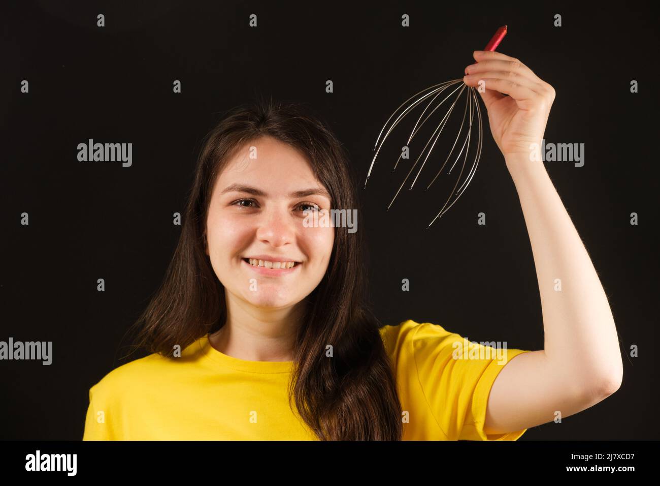 Eine Frau mit einem flexiblen Massagegerät aus Metall zur Selbstmassage des Kopfes auf schwarzem Hintergrund. Stockfoto