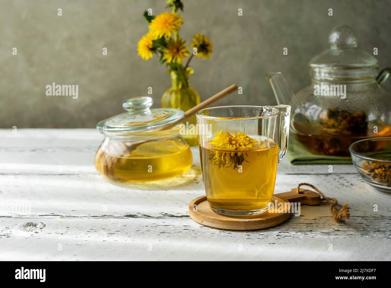 Dandelion Honig und Tee auf dem weißen Holztisch mit Teekocher, Dandelionblüten, trockener Kräutermischung zum Aufguss Stockfoto