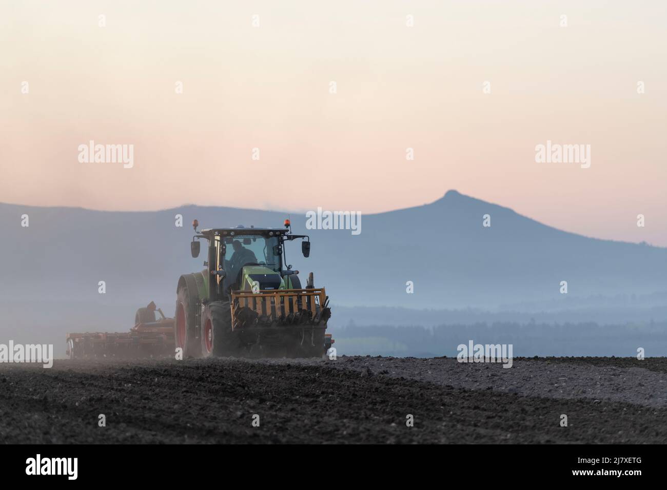 Ein Claas-Traktor, der abends in Aberdeenshire eine Scheibenegge über ein gepflügtes Feld schleppt, wobei Bennachie in der Ferne zu sehen ist Stockfoto