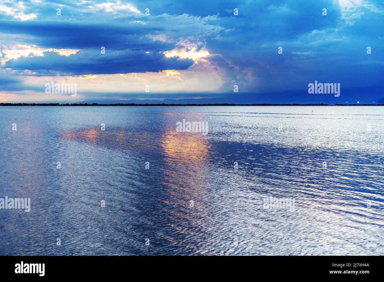 Schöner und friedlicher Sonnenuntergang über dem Meer mit blauen Wolken und orangefarbener Sonnenreflexion im Wasser Stockfoto
