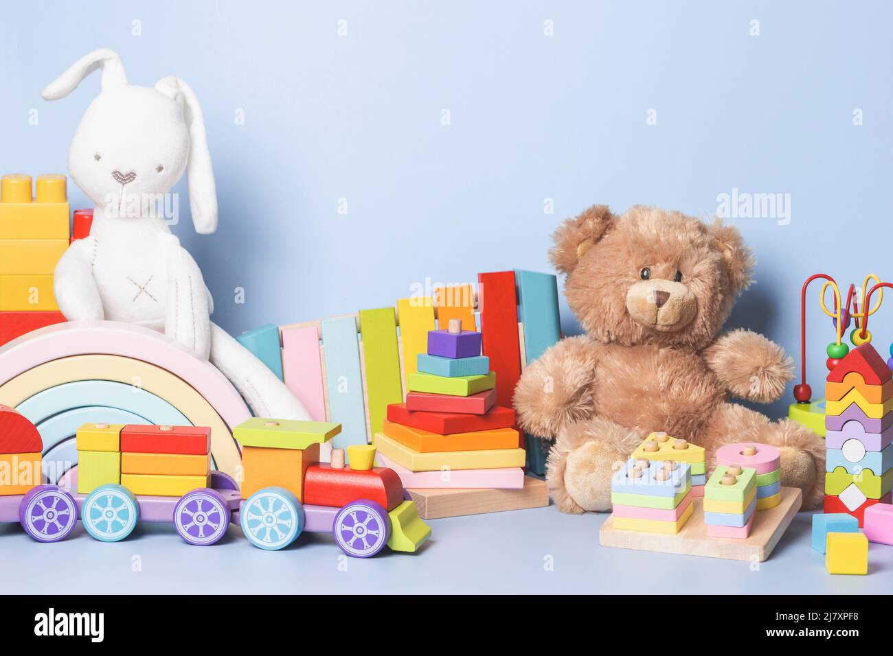 Kinder Spielzeug Sammlung isoliert auf blauem Hintergrund. Teddybär, weißer Hase, Holz, Kunststoff und flauschiges Lernspielzeug für Babys. Vorderansicht Stockfoto