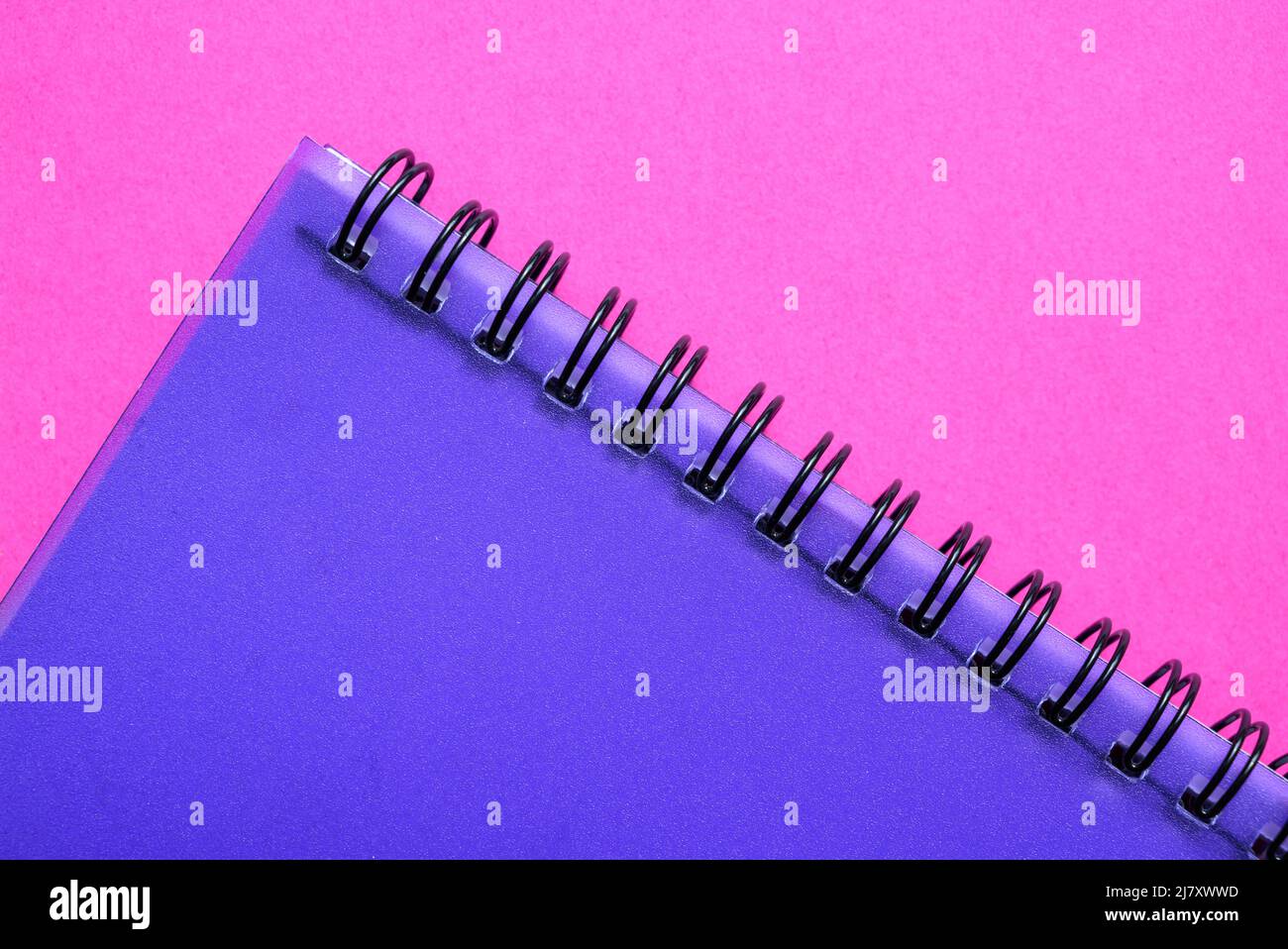 Teil eines drahtgebundenen (oder spiralgebundenen) Notizbuchs mit violettem, durchsichtigem Kunststoffdeckel auf rosa Hintergrund. Stockfoto