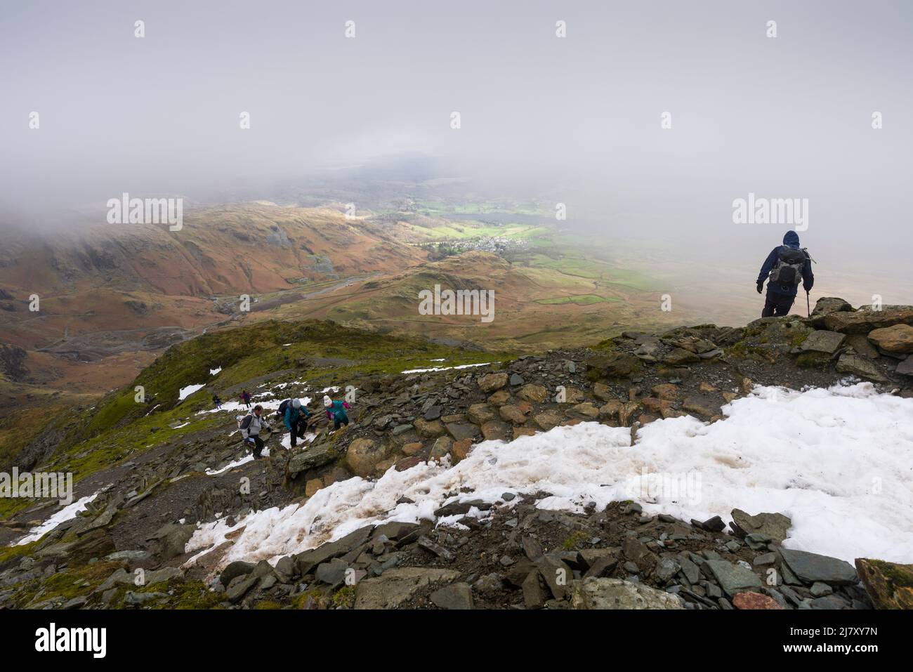 Wanderer, die im Spätwinter den Weg zum Gipfel des Old man of Coniston im Lake District National Park, Cumbria, England, besteigen. Stockfoto