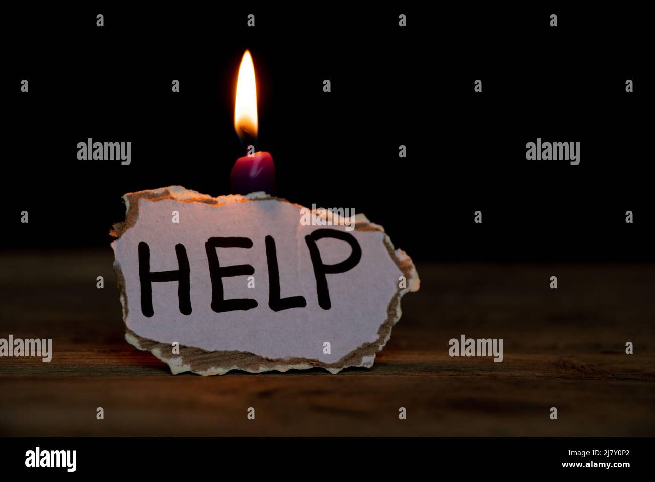 Papppapier mit Texthilfe steht bei einer Kerze im Dunkeln auf einem Tisch zu Hause, eine Nachricht über die Hilfe für die Ukraine im Krieg 2022 Stockfoto