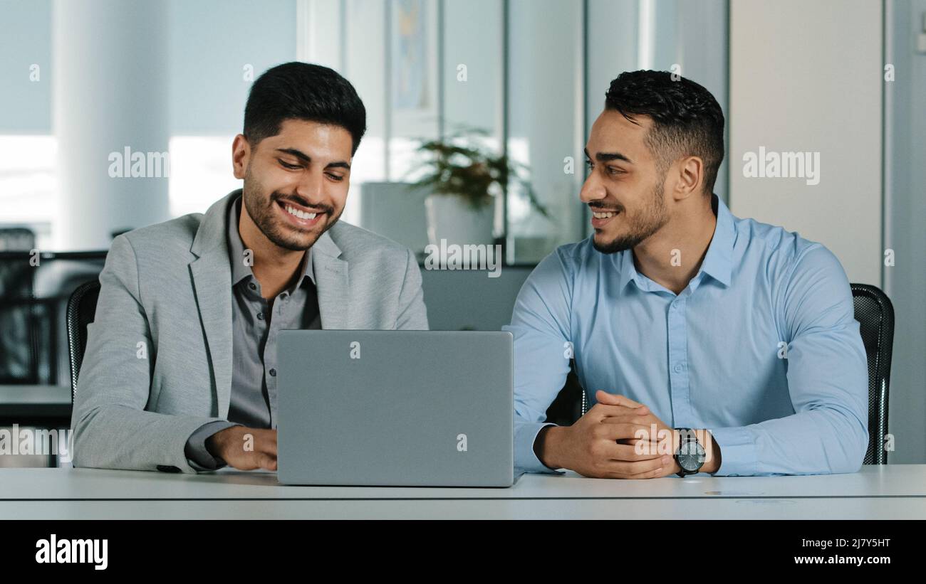 Überglücklich lächelnde männliche Mitarbeiter schauten auf den Laptop-Bildschirm und waren begeistert von unglaublichen guten Nachrichten. Glückliche Mitarbeiter feiern, dass sie angezogen werden Stockfoto