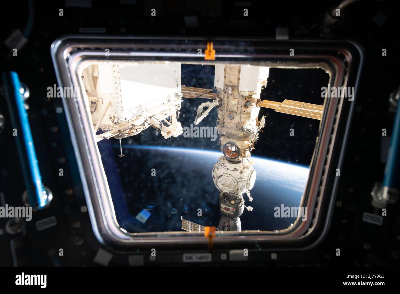 Ein Blick aus einem Fenster auf die Kuppel der Internationalen Raumstation auf die russischen Komponenten, darunter (von unten) das Sojus MS-21-Besatzungsschiff, das Pritschal-Andockmodul und das Nauka-Mehrzweck-Labormodul, 4. Mai 2022 in Earth Orbit. Stockfoto