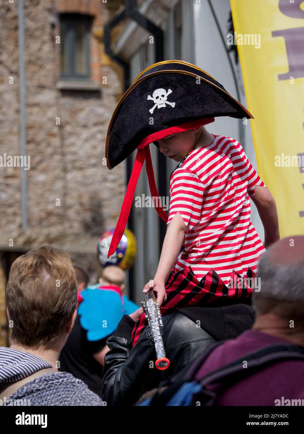 Kleiner Junge in Piratenkostüm, der auf den Schultern des Vaters beim Brixham Pirate Festival 2022 in Devon, Großbritannien, getragen wird Stockfoto