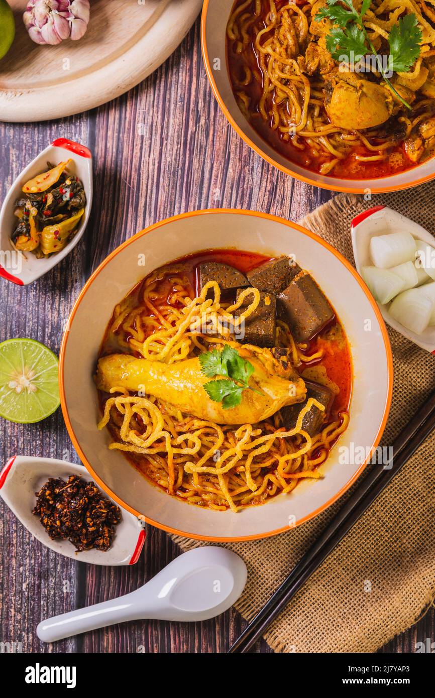 Khao Soi Kai, Blick von oben, köstliches nordthailändisches Essen, mit Gewürzen auf dem Tisch arrangiert. Stockfoto