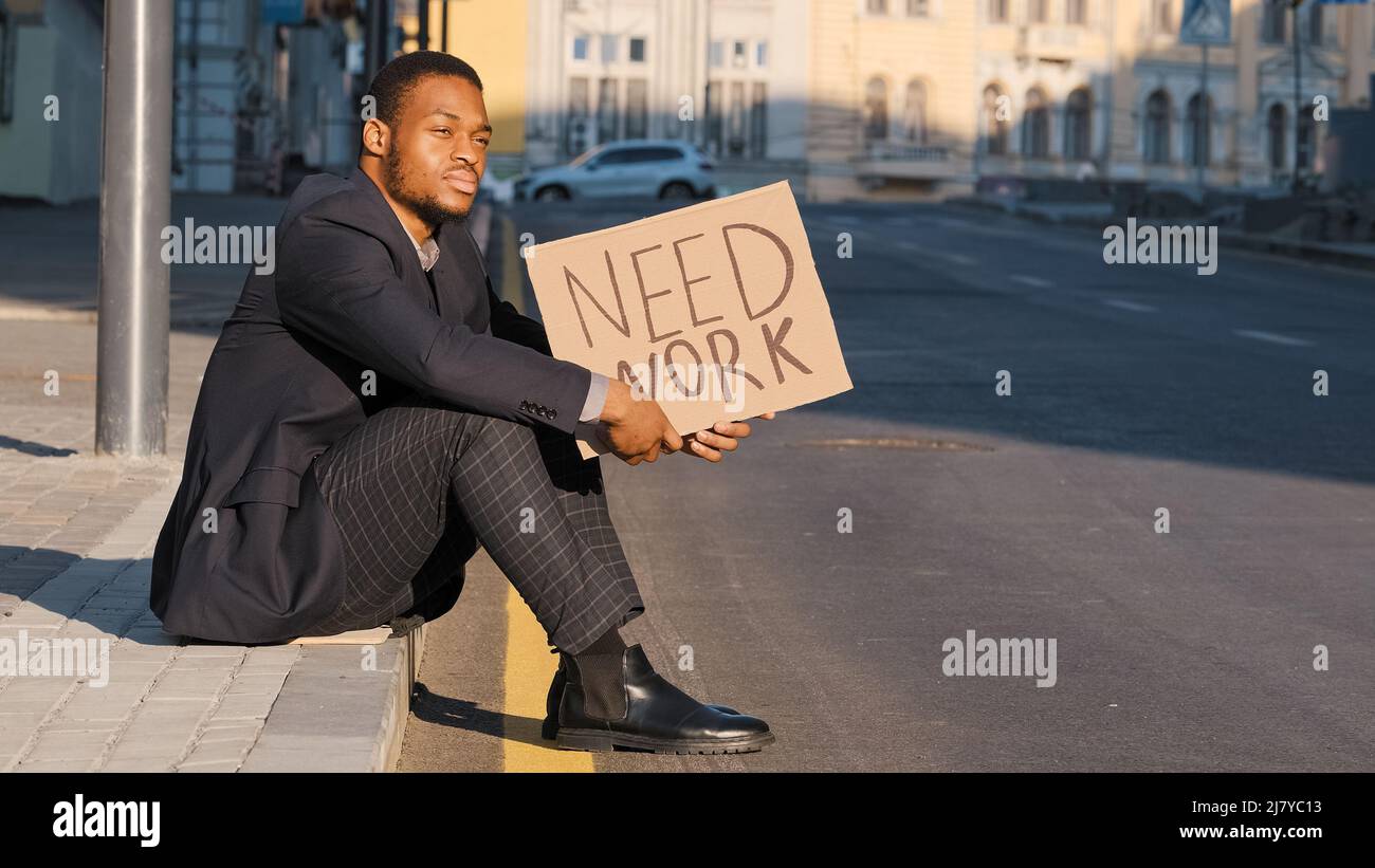 Verzweifelte verärgerte afroamerikanische Millennial Student trägt Anzug sitzen auf Treppen im Freien halten Plakat brauchen Arbeit, schwarzer Geschäftsmann nervös Stockfoto