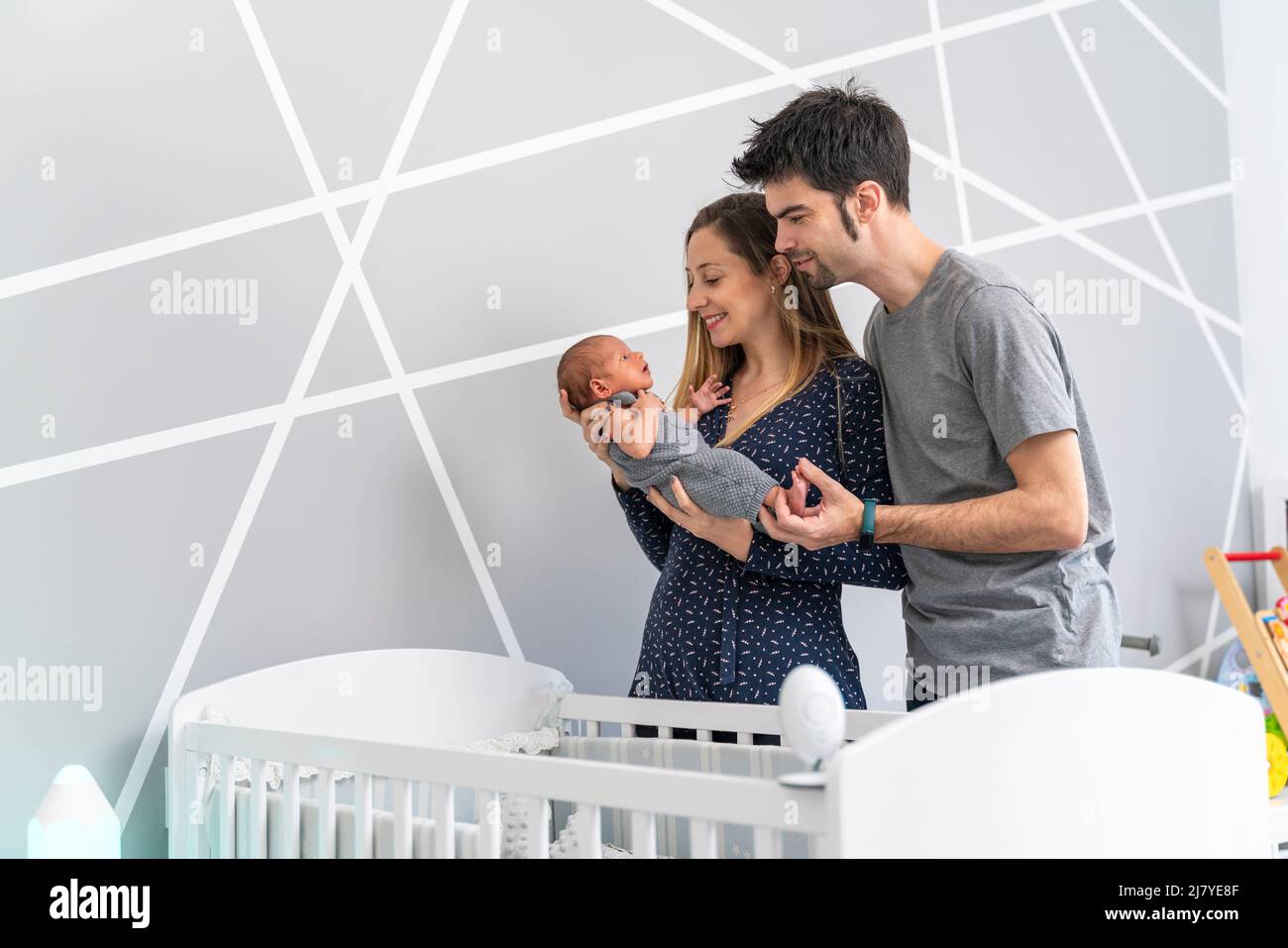 Junge Eltern mit ihrem Baby in den Armen in der Nähe der Krippe im Schlafzimmer Stockfoto