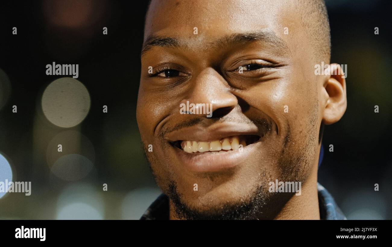 Männlich glücklich Porträt afroamerikanischen jungen Millennial zufrieden Mann steht in der Stadt in Abend Stadt Lichter Hintergrund Blick auf Kamera lächelnd toothy Stockfoto