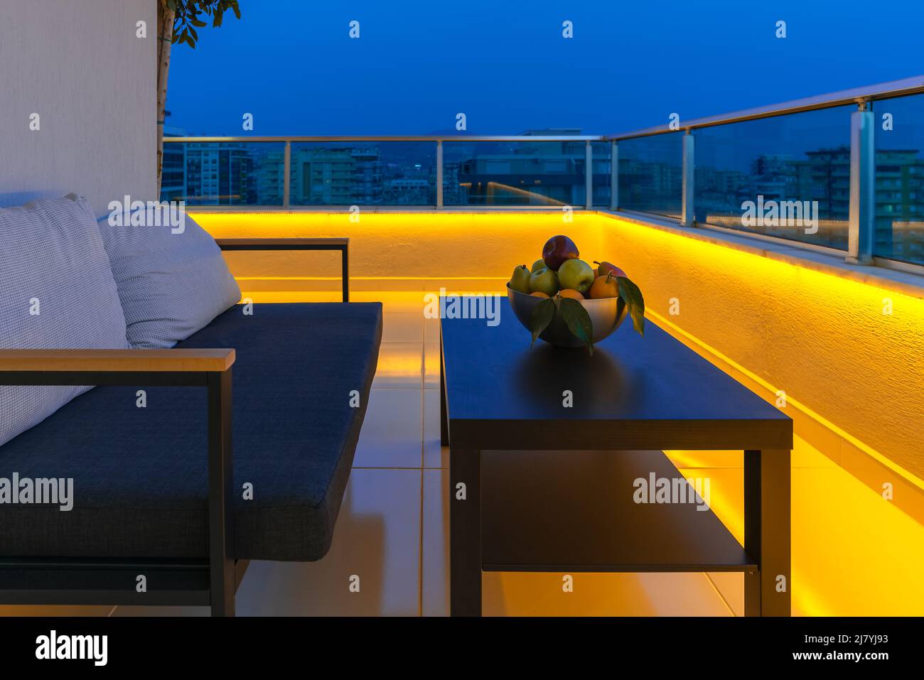 Blick auf eine gemütliche Außenterrasse mit Sessel, Couchtisch und Obstschale, LED-Beleuchtung am Abend. Stockfoto
