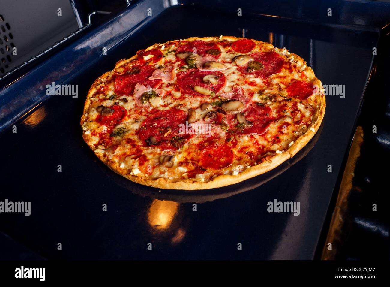 Frau öffnet Öfen und nehmen Sie Pizza mit Tomaten, Oliven, Pilzen und Käsewurst Stockfoto