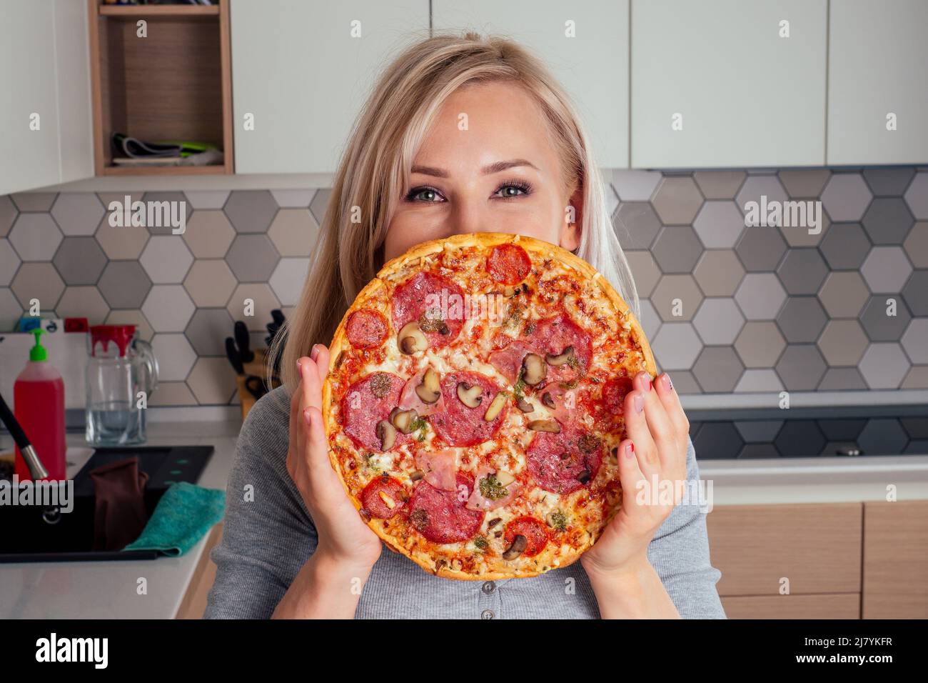 Frau öffnet Öfen und schneidet Pizza mit Tomaten, Oliven, Pilzen und Käse Wurst Stockfoto